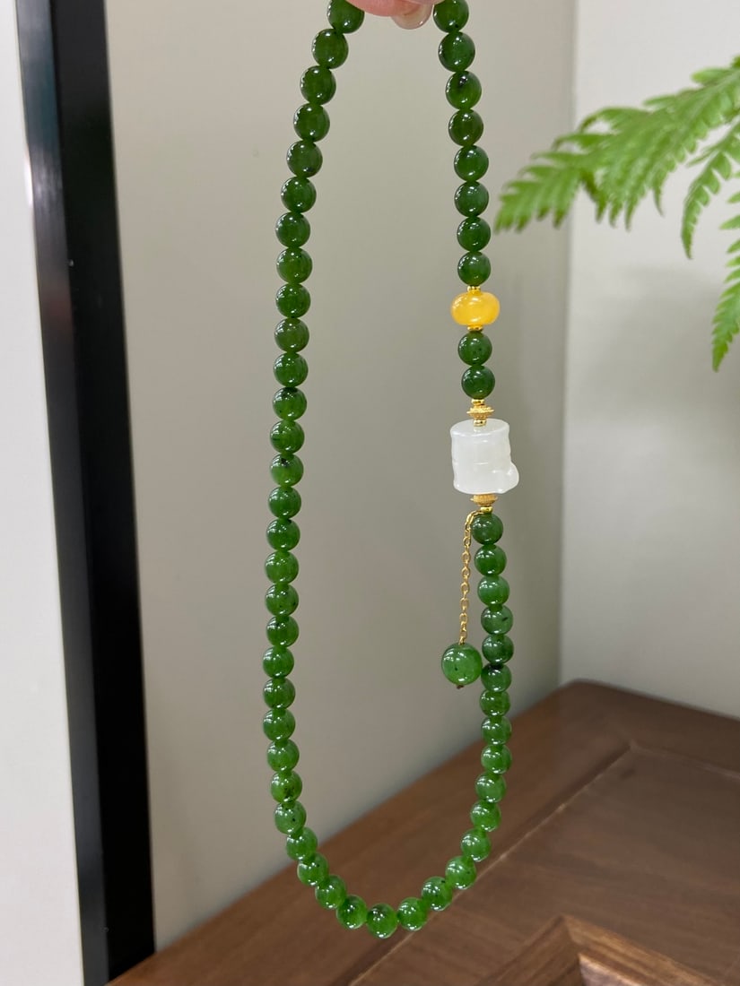 A Finely Carved Hetian Jade Spinach-Green Double-Strand Bracelet: A finely carved Hetian jade bracelet of spinach-green quality, composed of 6mm beads, accompanied by white jade and amber beads. The bracelet measures 6mm in bead diameter. 和田玉