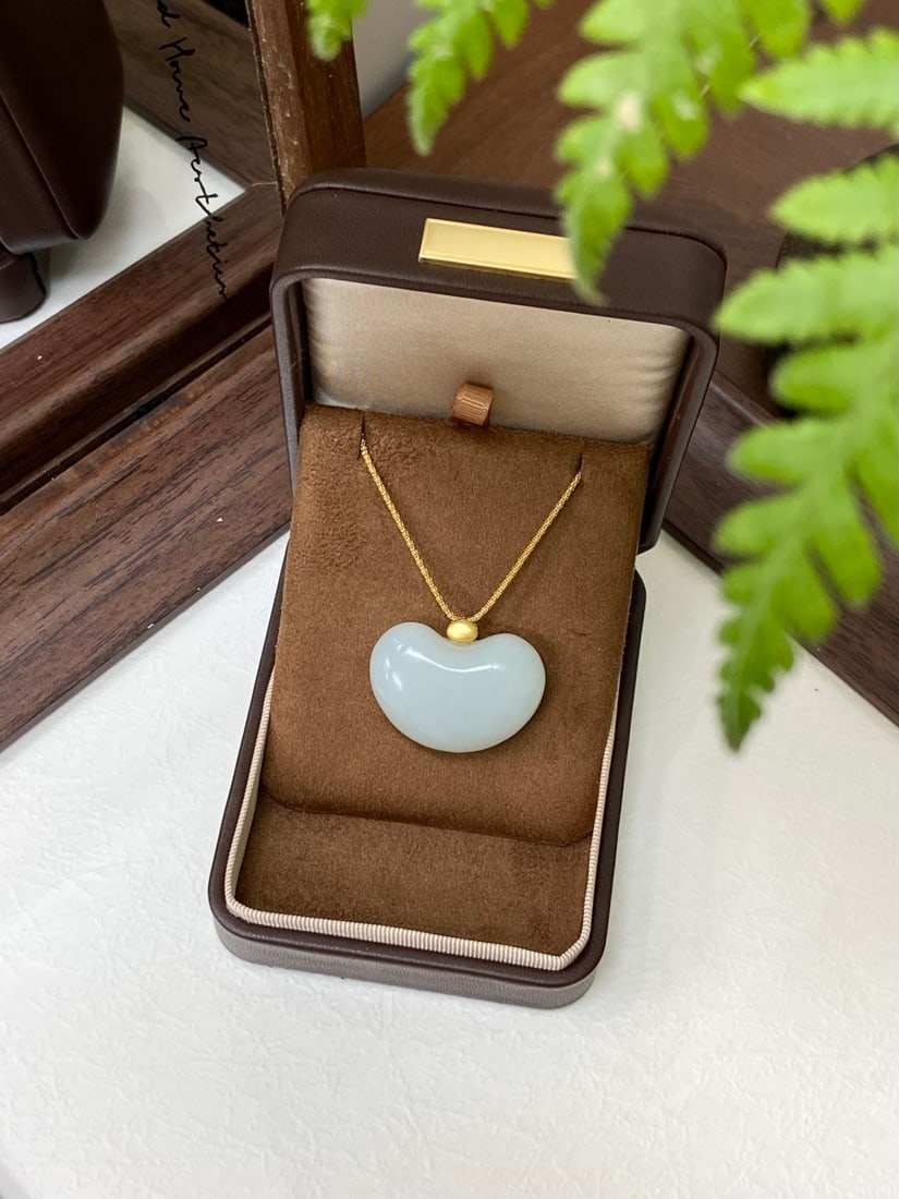 A Finely Carved Hetian Jade 'Bean' Pendant: A finely carved Hetian jade pendant of white tone, carved as a bean (fudou), a symbol of blessing and prosperity, set in 18K gold. The pendant measures 33.6mm by 23.5mm by 12.8mm. 和田