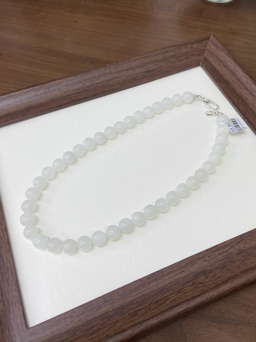 A Finely Carved Hetian Jade White Jade Necklace: A finely carved Hetian jade necklace of white quality, composed of round beads of 12mm diameter. The jade is of fine, warm texture with a smooth, luminous finish. The necklace measures 12mm in bead