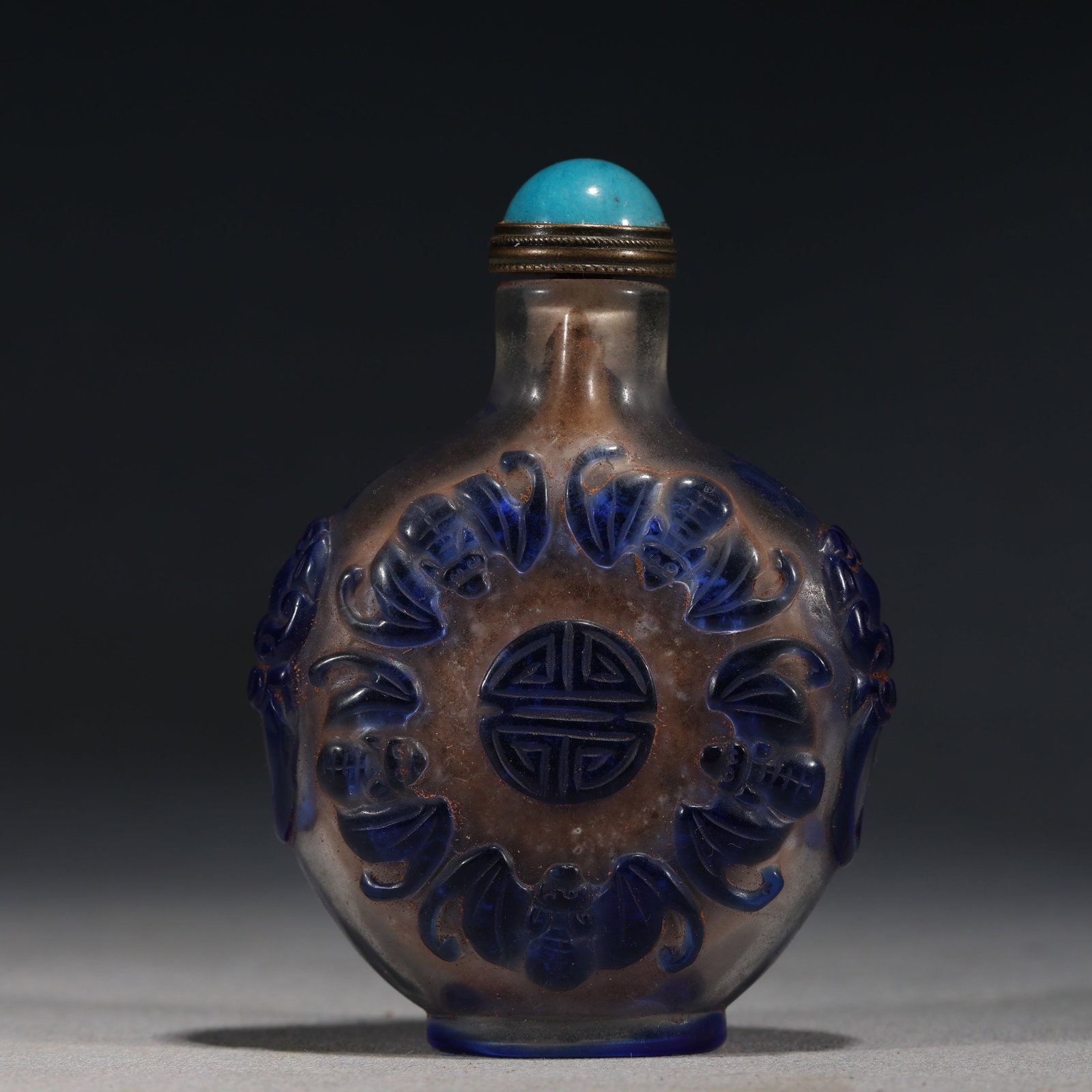 A Chinese Blue Overlay Glass Snuff Bottle with Shou Character,Guangxu Mark: A blue overlay glass snuff bottle,carved with a stylized shou character within a geometric border.Fitted with a turquoise stopper.The base bears a four-character regular script mark reading Guangxu Ni