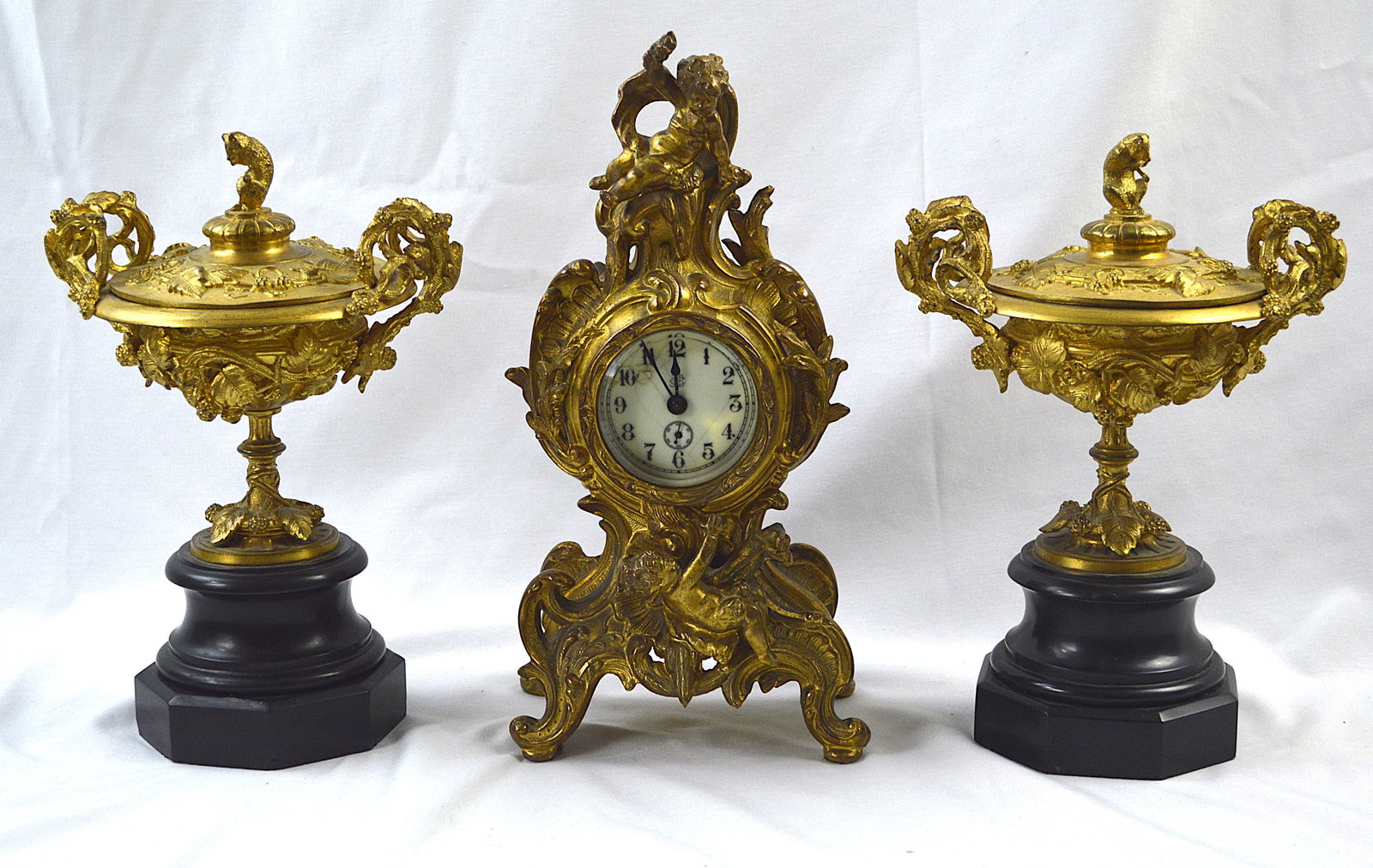 Gilt Louis XV Clock Garniture Set: Gilt bronze Louis XV clock and garniture set (three pieces in total). Clock circa 1920s Jennings Bros, Connecticut. Measures: Clock is 12 inches high and garnitures (on marble base) are 11 inches in h