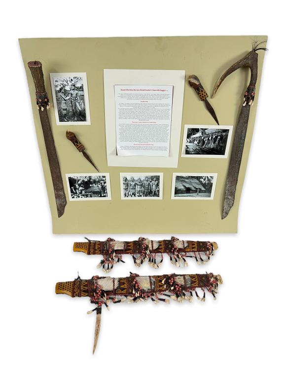 (2) Antique Dayak Mandau Swords W/ Daggers: Each sword measures approx 25" long including handle. Sheaths are painted wood, fur, teeth, beads, & rope. Swords, daggers, photos, & paperwork is laid on poster board.