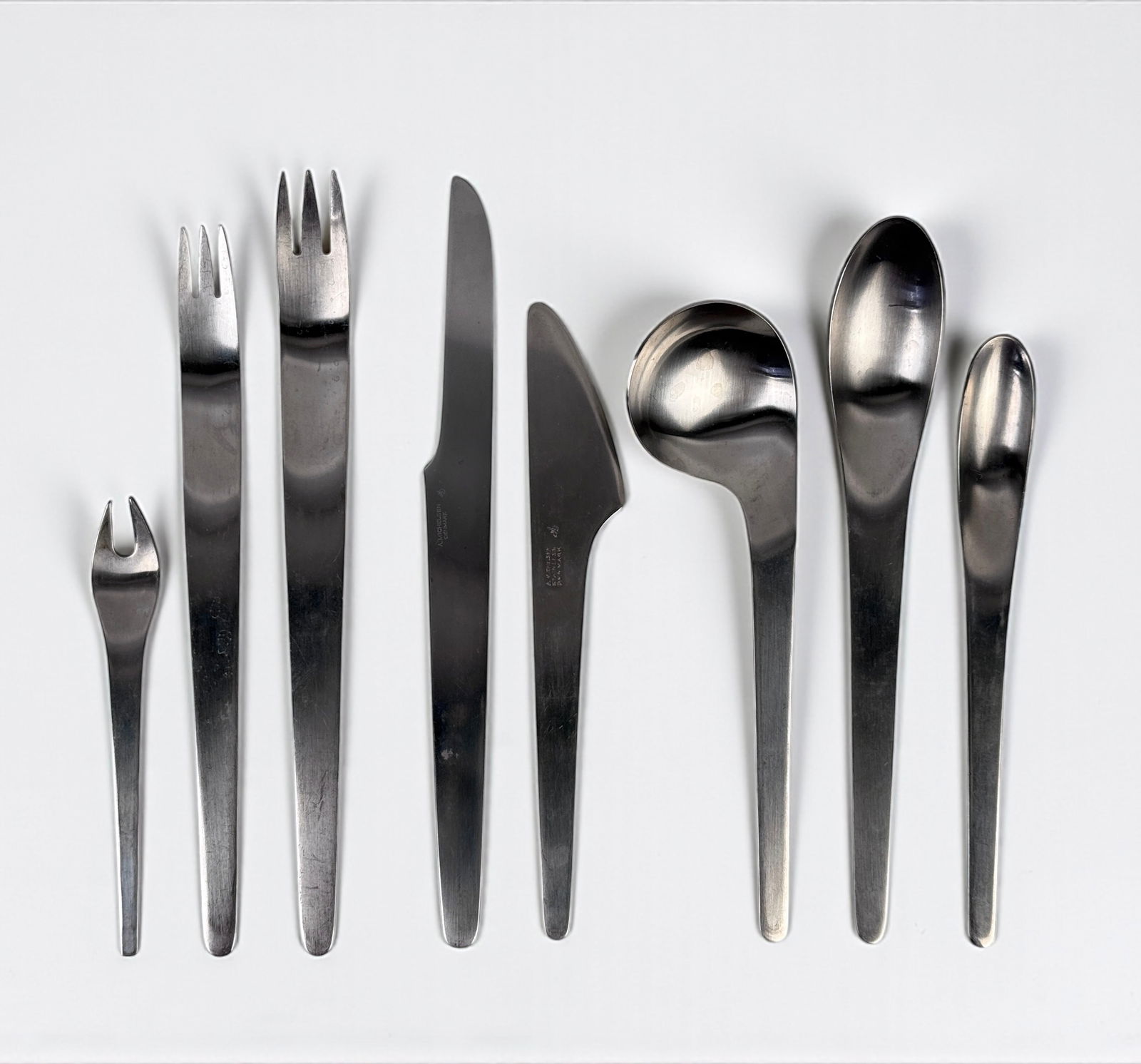 (110 pc) Arne Jacobsen Stainless Steel Flatware Set: For A. Michelsen Denmark Set includes: (12) Long Knives- 7 3/4" (13) Short (Butter) Knives- 6 1/2" (12) Dinner Forks- 7 3/4" (11) Salad Forks- 7 1/2" (12) Cocktail Forks