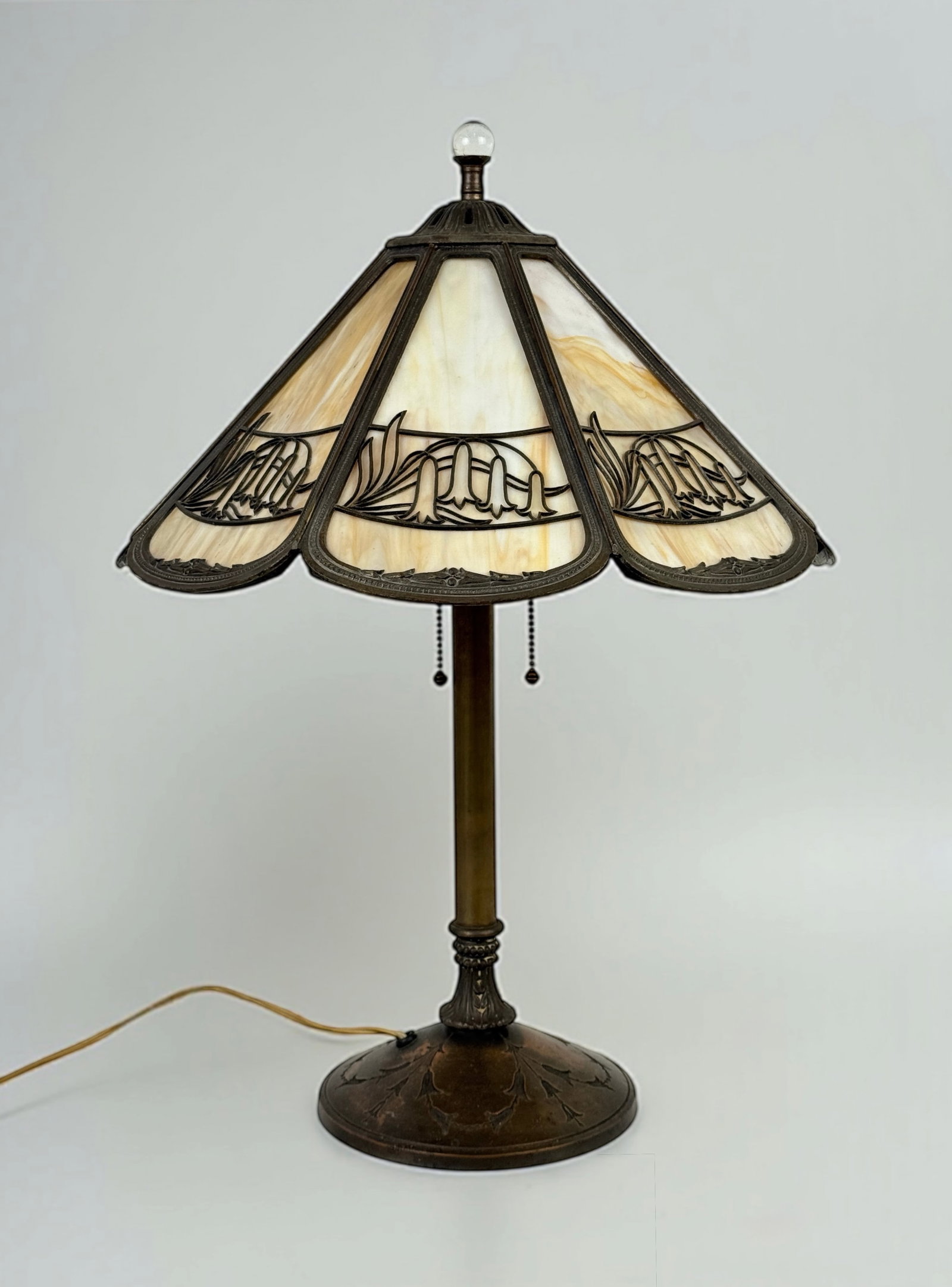 Slag Glass Table Lamp with Floral Metal Overlay: Height: 24” Condition: There is a crack in one of the glass panels, and a few pieces of the pierced metal overlay are missing. Light surface wear and patina to the base. Lamp is in w