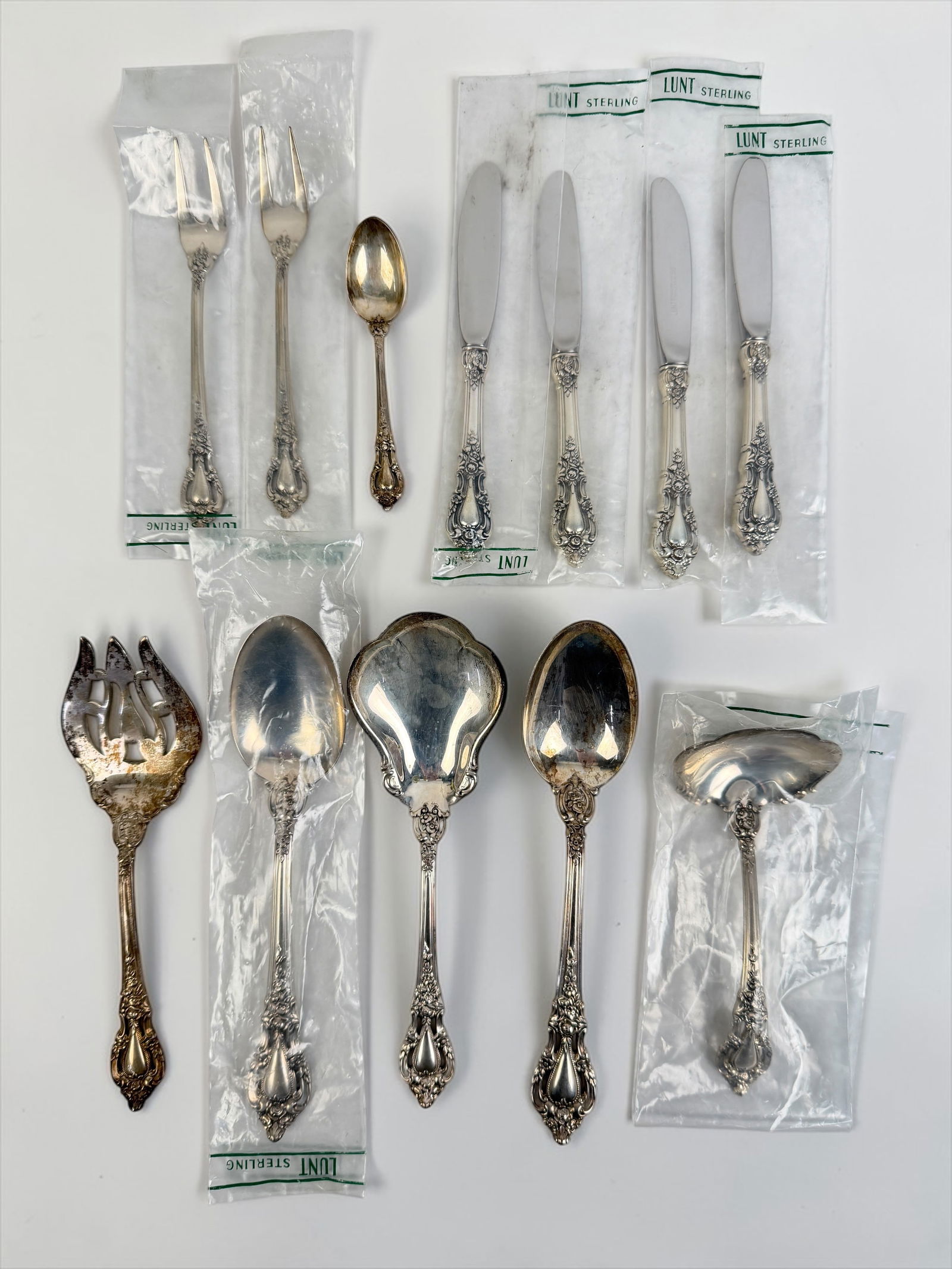 (12) Lunt Eloquence Sterling Serving Pieces: (3) Various Serving Forks(4) Various Serving Spoons(1) Demitasse Spoon(4) Butter Knives Total Weight: 16.3ozt PLUS (4) Sterling Handled Knives Condition: Various levels of tarnishing. Most