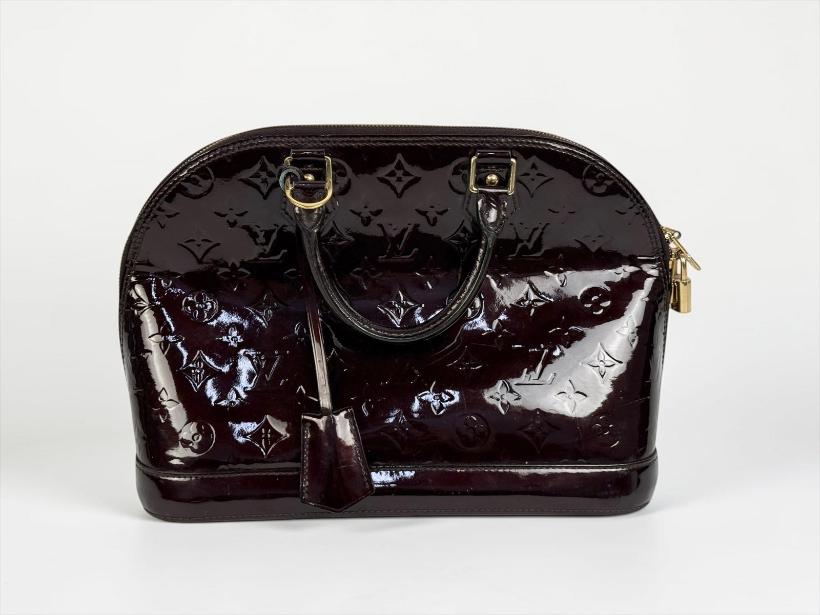 Louis Vuitton Vernis Alma BB Burgundy Handbag: Monogram Vernis with brass hardware. Canvas interior with dual interior pockets. Includes Louis Vuitton lock and key. Dimensions: 9" x 12" x 6" Condition