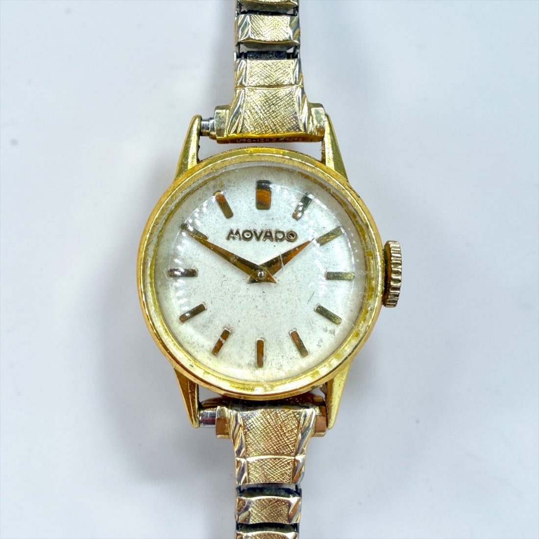 18K Movado Ladies Watch: Face: 17.4mm Diameter Band: 5.75" Note: only the watch is gold, not the band. Condition: Scratches to the crystal and casing. Minor wear to the band. Not tested for time keeping.&nbs