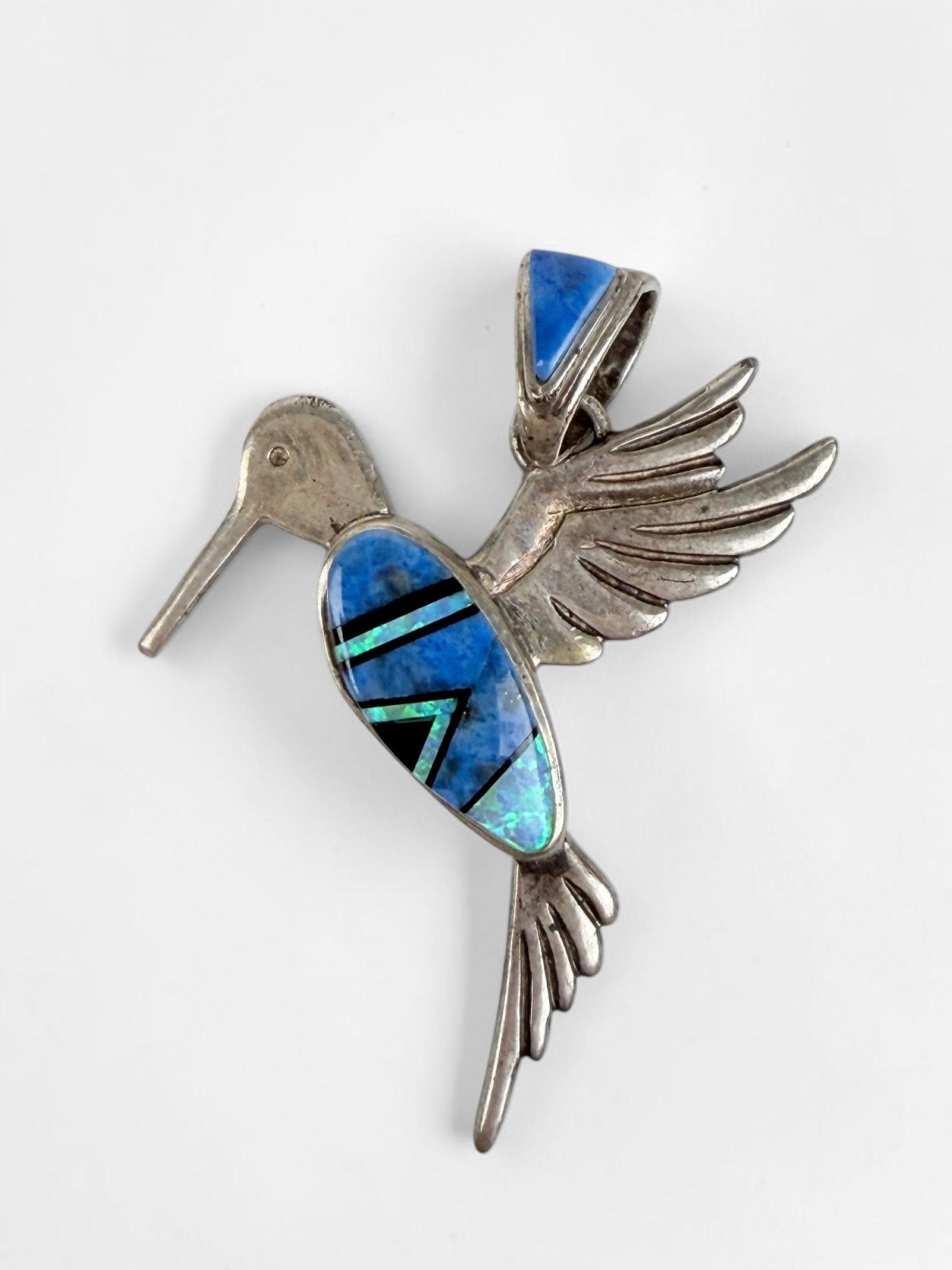 Calvin Begay Sterling & Multi-Stone Inlaid Hummingbird Pendant: Signed by the artist on reverse. Dimensions: 2 3/4" x 1 1/2" Total Weight: 6.9g Condition: The pendant is in good condition. See images for details. 