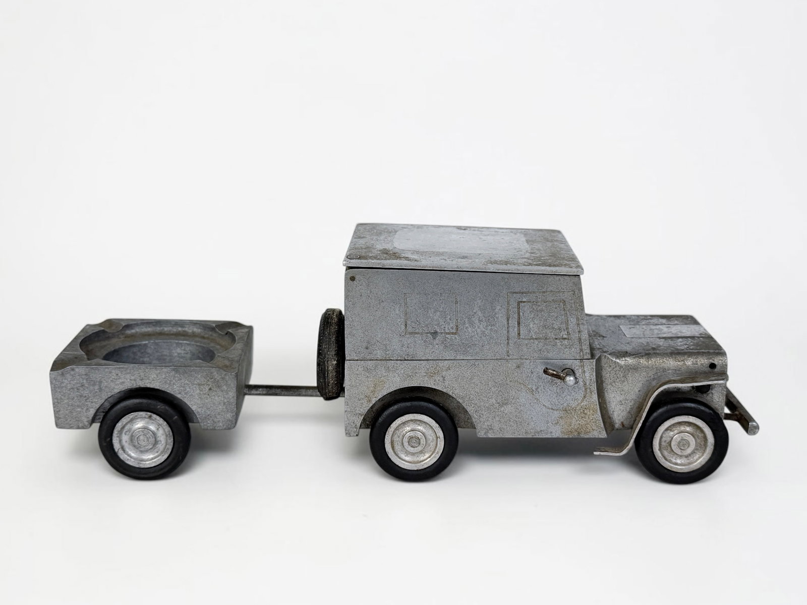Vintage Baier WWII German Jeep Smoker's Companion Set: The aluminum Jeep functions as a cigarette box and lighter, while the accompanying trailer is an ashtray. Dimensions: 3" x 9 1/2" Condition: Wear throughout the set