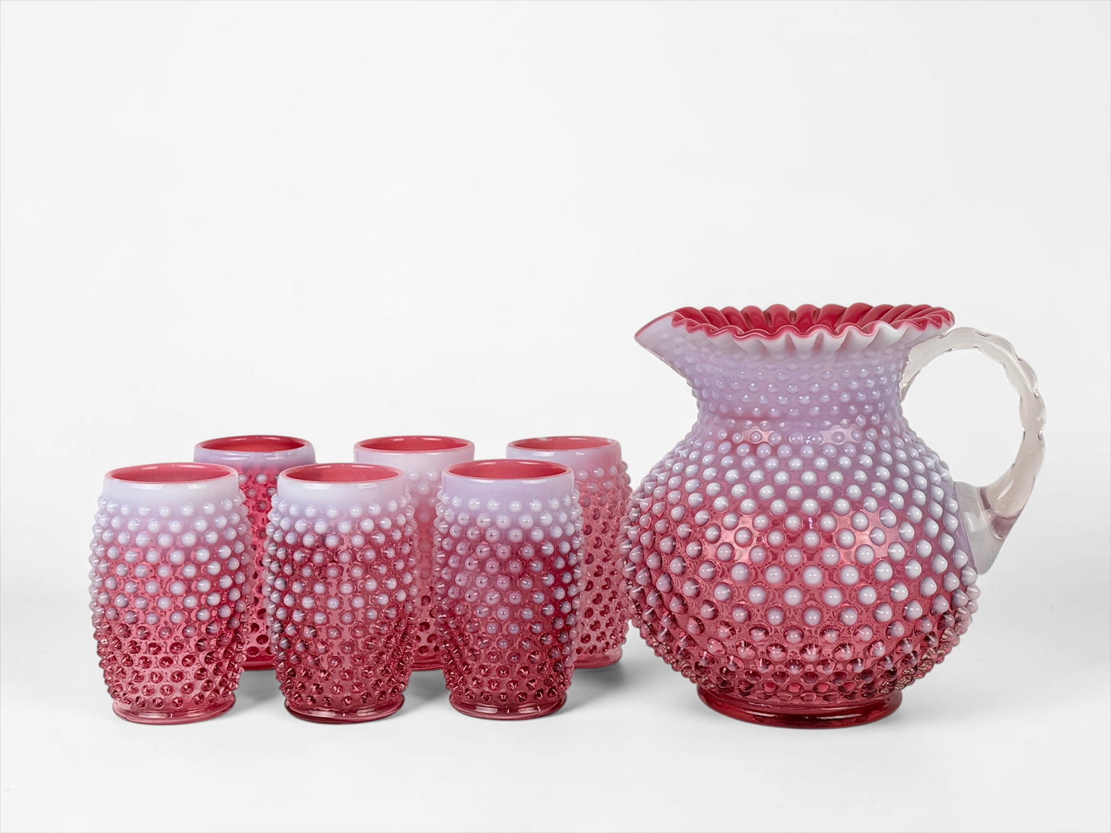 (7pc) Pink Fenton Pitcher and Glass Set: Set includes (1) pitcher and (6) cups. Pitcher: 7 1/2" Tall x 8" Widest Point Cup: 4 3/4" Tall x 3" Wide Condition: The set is in good condition. Please