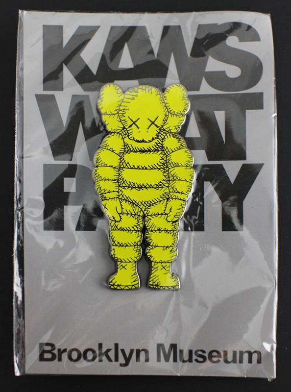 KAWS (American, b.1974) "What Party?" yellow small pin, brand new, 2 3/4 x 1 1/4 in. (1 of 2)