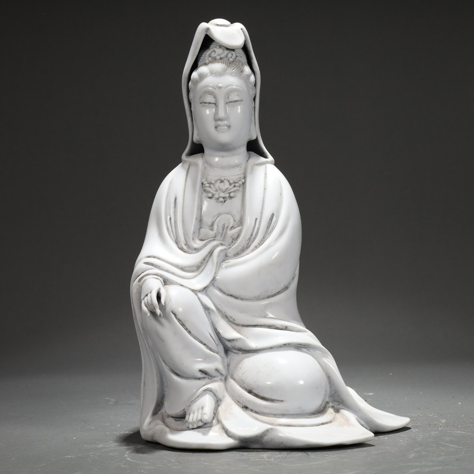 An Exquisite Blanc-De-Chine Figure Of Avalokiteshvara Seated On A Rock: An Exquisite Blanc-De-Chine Figure Of Avalokiteshvara Seated On A Rock. The figure is seated, body rendered clad in long, flowing robes, the voluminous drapery elegantly cascading in folds. Chinese Mi