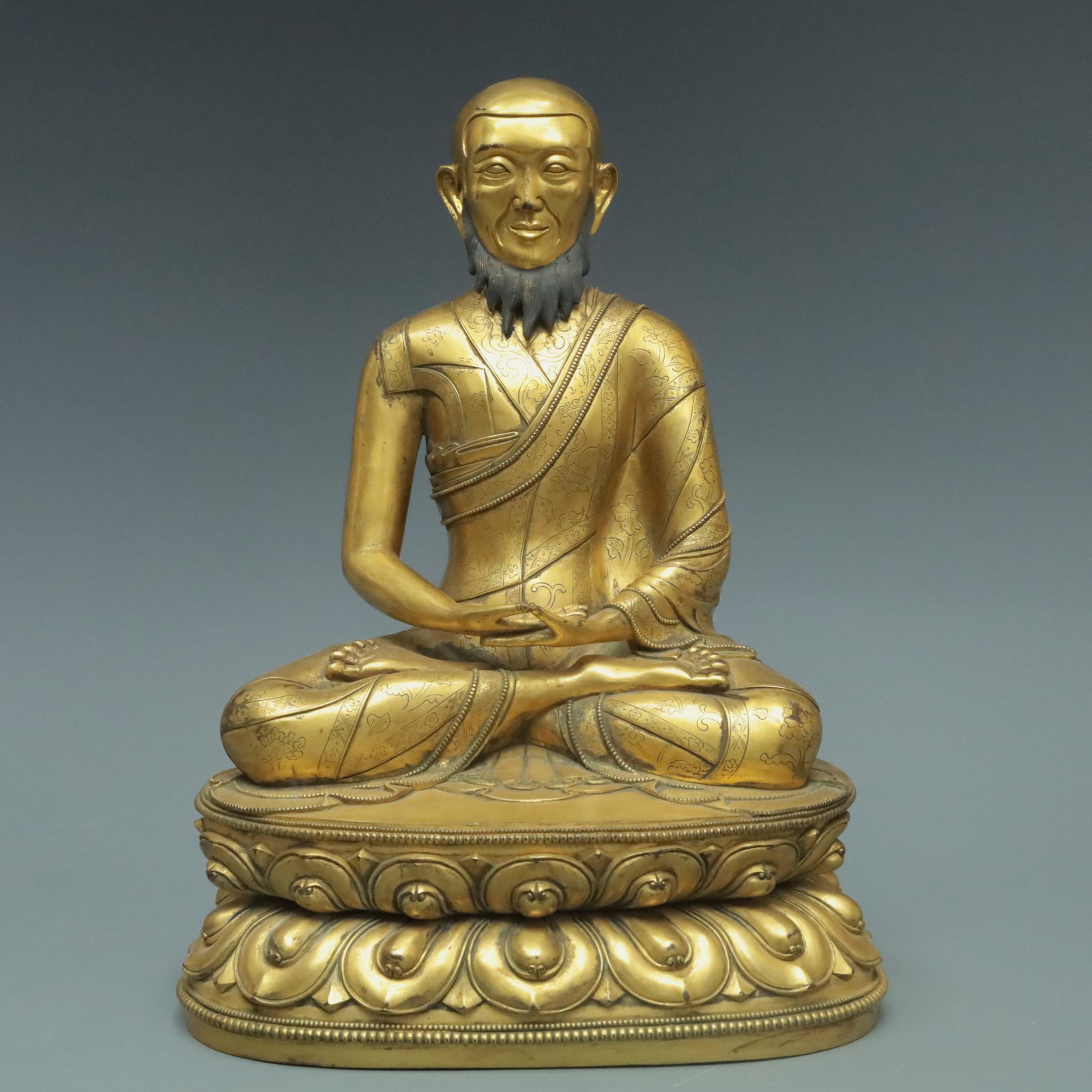 A Magnificent Gilt-Bronze Figure Of Mahasiddha: A Magnificent Gilt-Bronze Figure Of Mahasiddha. The figure with a composed expression is seated on a double-lotus base, body rendered clad in long, flowing robes, the voluminous drapery elegantly casc
