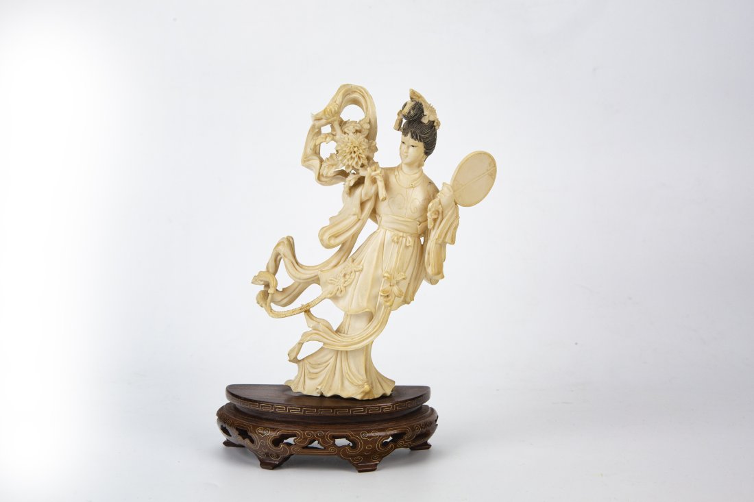 Bone Carved Goddess Statue with Stand: ChinaDimensions: 7 1/8" (18.1cm) Hwith standStatue of a goddess carved in bone, holding a round fan in her left hand and a bouquet of flowers in her right hand, with her face facing slightly to the lo