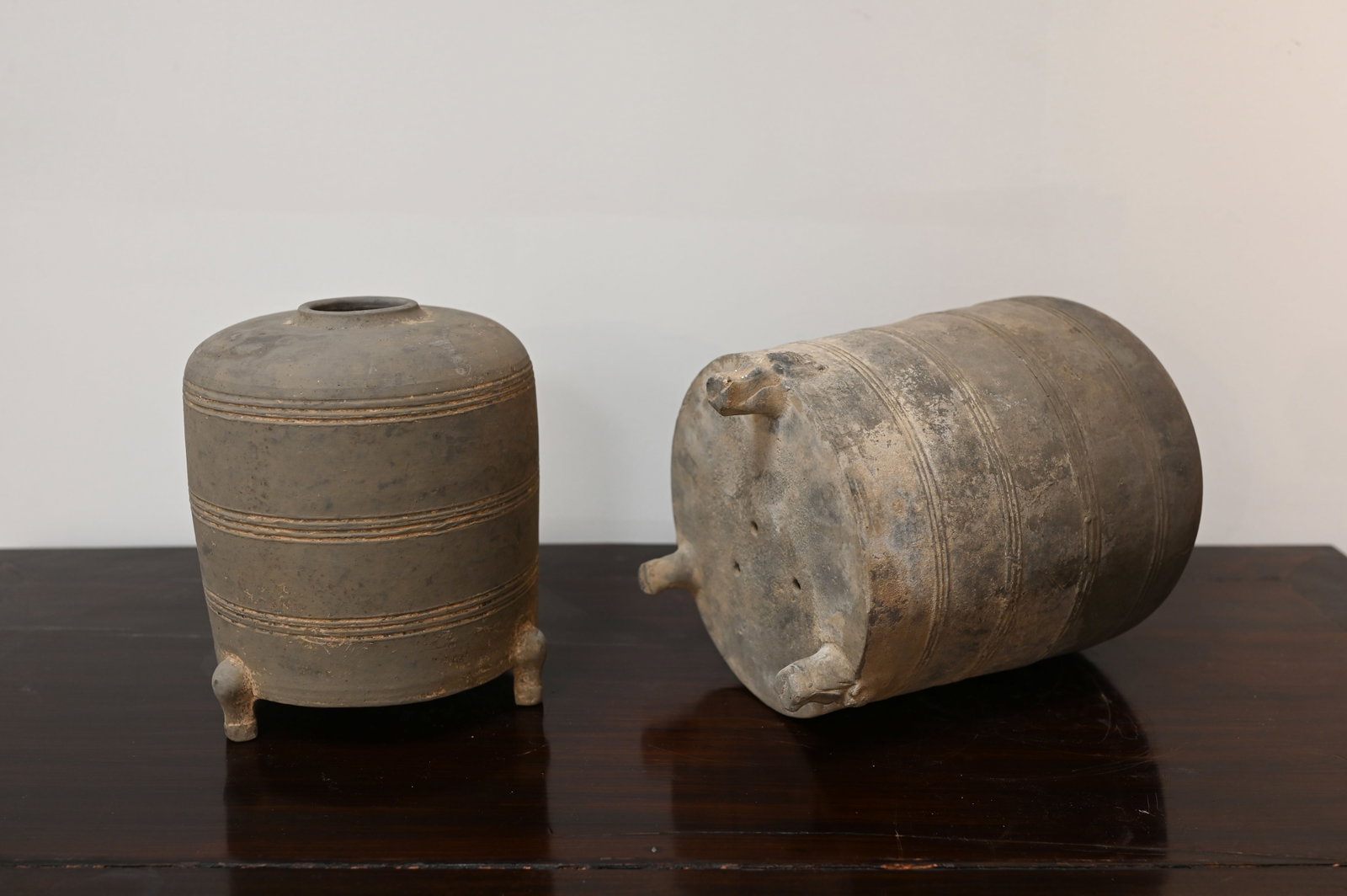 2 Archaistic Incised Pottery Granary Jars, Han Dynasty: Dimensions:A: 12" (30.5cm) HB: 9.5" (24cm) HA pair of stoneware tripods with short feet. Circular opening at the top and small rectangular opening at the lower base of the body. Minimal ornament with 