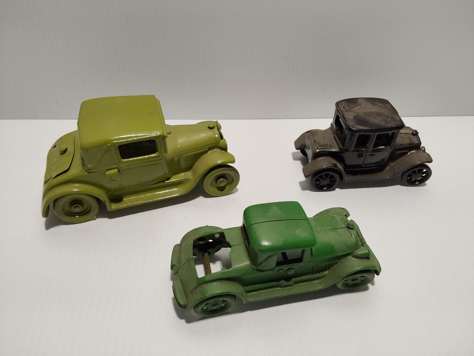 (3) cast iron toys: Olive green Arcade car (trunk has been replaced) - 6 1/2" long Black Arcade car - 5" long Green car (has missing trunk) - 6" long