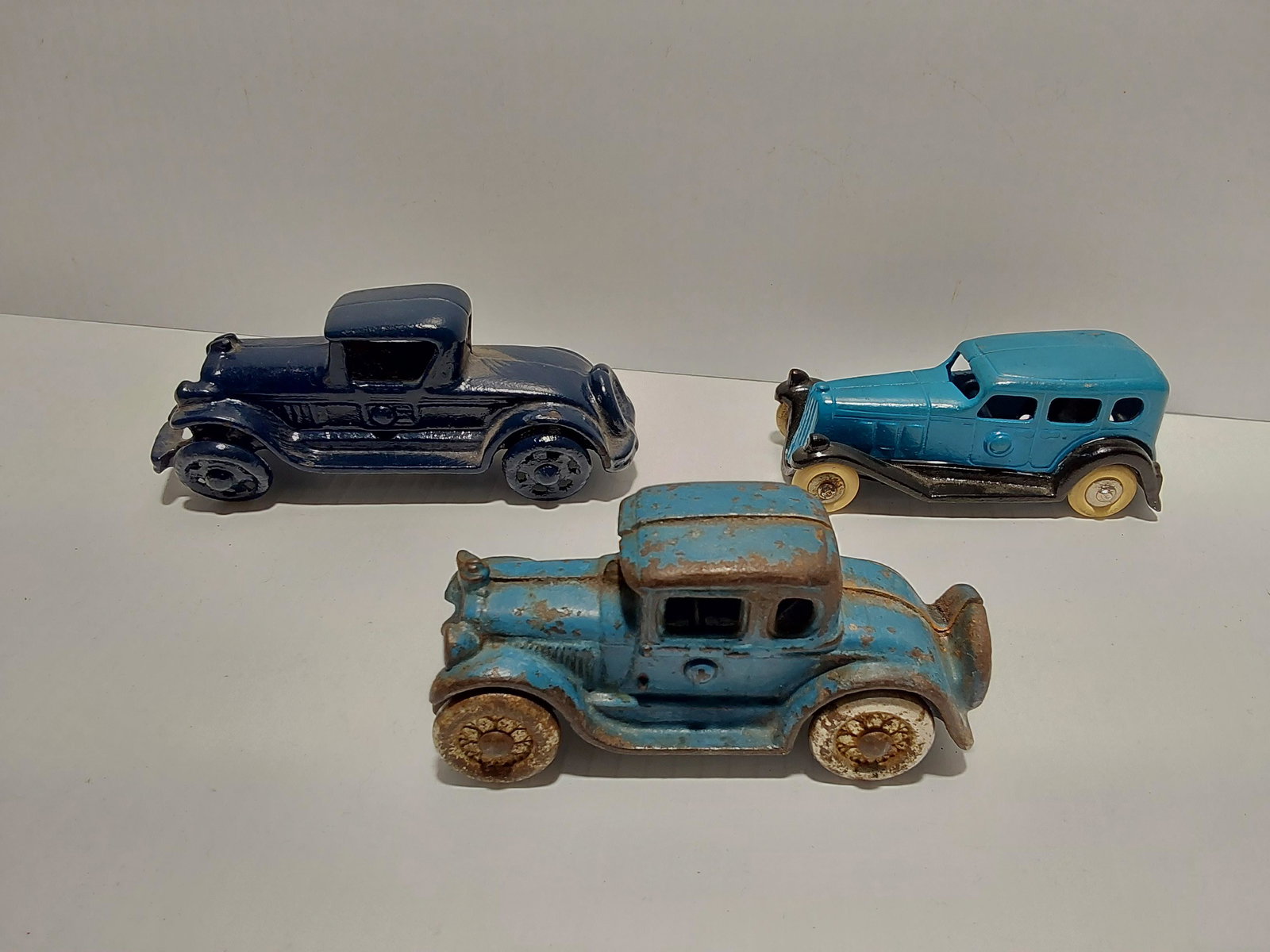 (3) cast iron toys: Dark blue car - 5" long Repainted car - 4" long Other car - 4 1/4" long