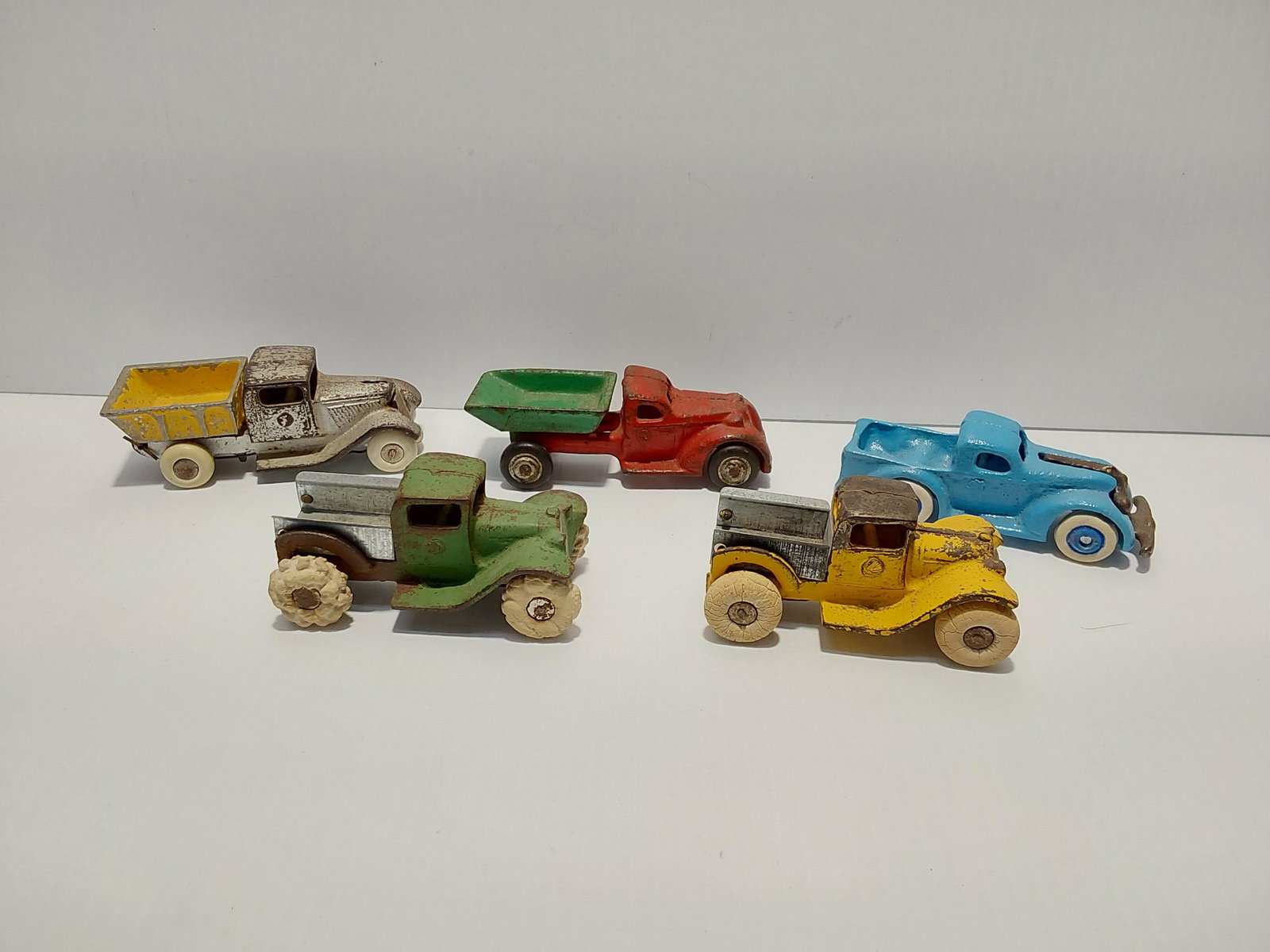 (5) cast iron toys: (2) dump trucks - 4" long Blue pickup - 4" long Green & yellow trucks (the beds have been replaced - 3 1/2": long