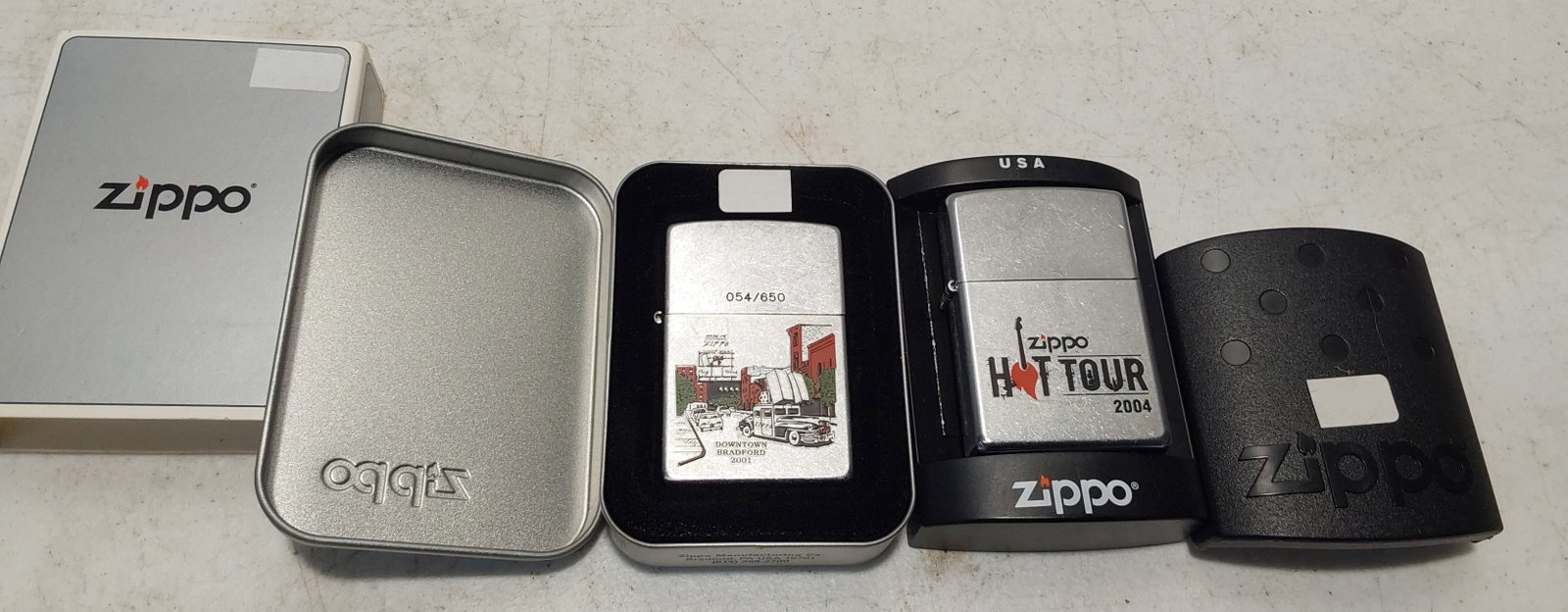 (2) unused collectible Zippo lighters: (1) 2004 Hot Tour on Street Chrome finish Zippo lighter in box with sleeve. Unused. (1) 2001 Downtown Bradford Street Chrome finish Zippo lighter in box with sleeve. #054 of 650. Unused.