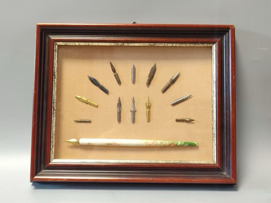 A vintage framed antique painting with a dipping pen hanging from Italy: This calligraphy and painting pen tip display is composed of multiple pen tips of different materials and shapes arranged in combination, accompanied by a brush body. The overall layout is elegant, re