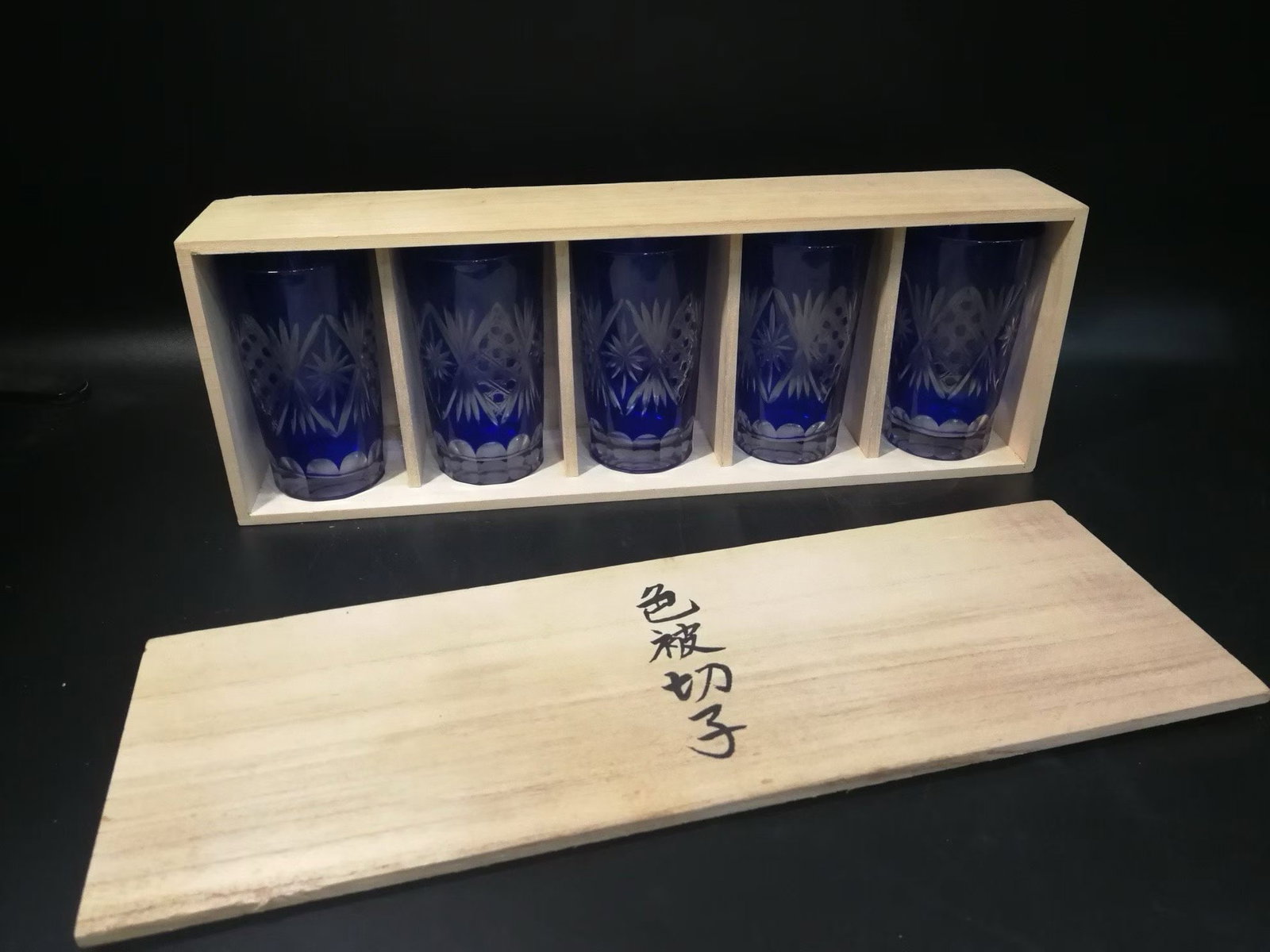 A set of original box color cut wine glasses: A set of five blue glass cups with original wooden packaging box. The cup body has a deep blue transparent texture, decorated with carved patterns, and has an elegant shape. The overall packaging size