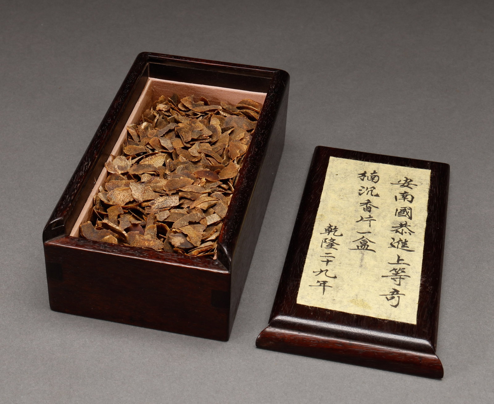 A box of Qing Dynasty Qinan agarwood slices: A wooden box is used to hold one piece of agarwood. The box body is made of dark wood and contains agarwood slices inside. The box cover is decorated with inscriptions, featuring traditional incense c