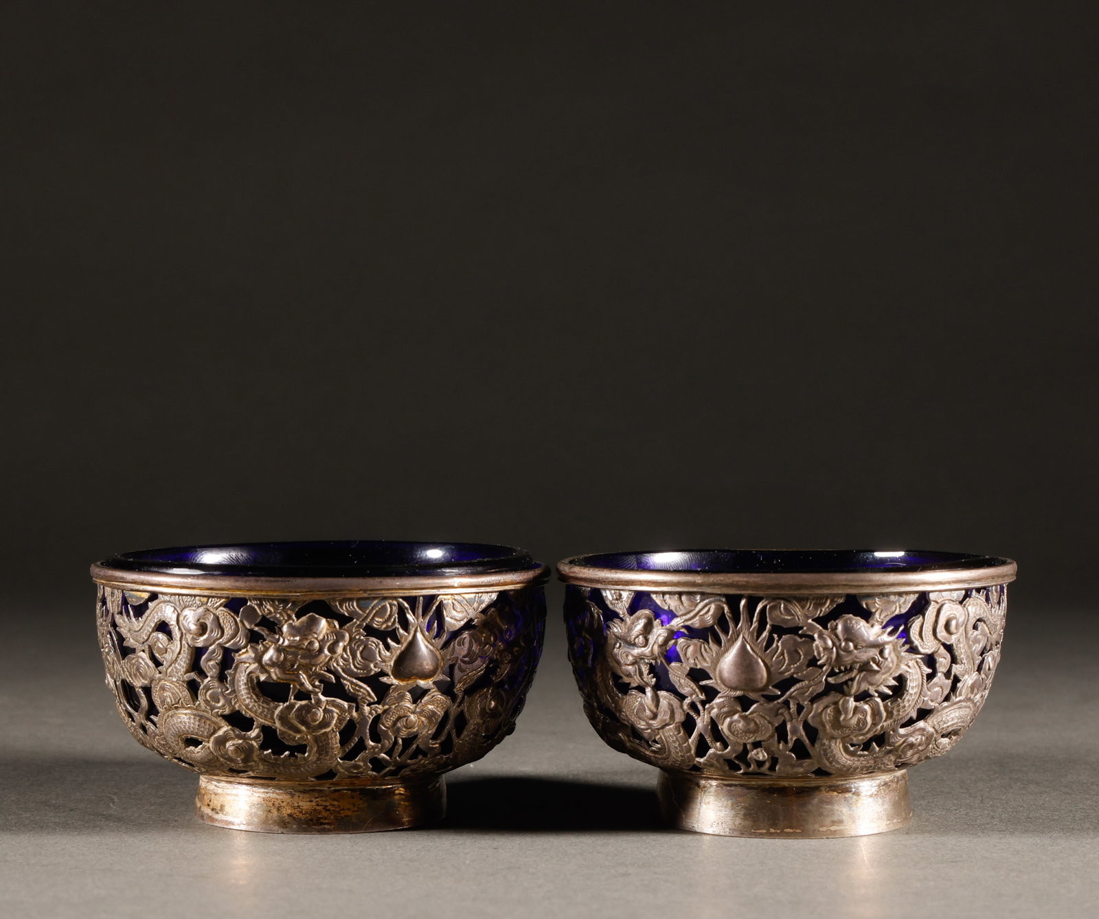 A pair of silver bowls with double dragon patterns from the Qing Dynasty: Old silver hollowed out double dragon pearl patterned blue glass inner pot tea cup pairSpecification: 4.5cm in height and 8cm in diameter, with a total weight of 311g. The silver shell is carved with 