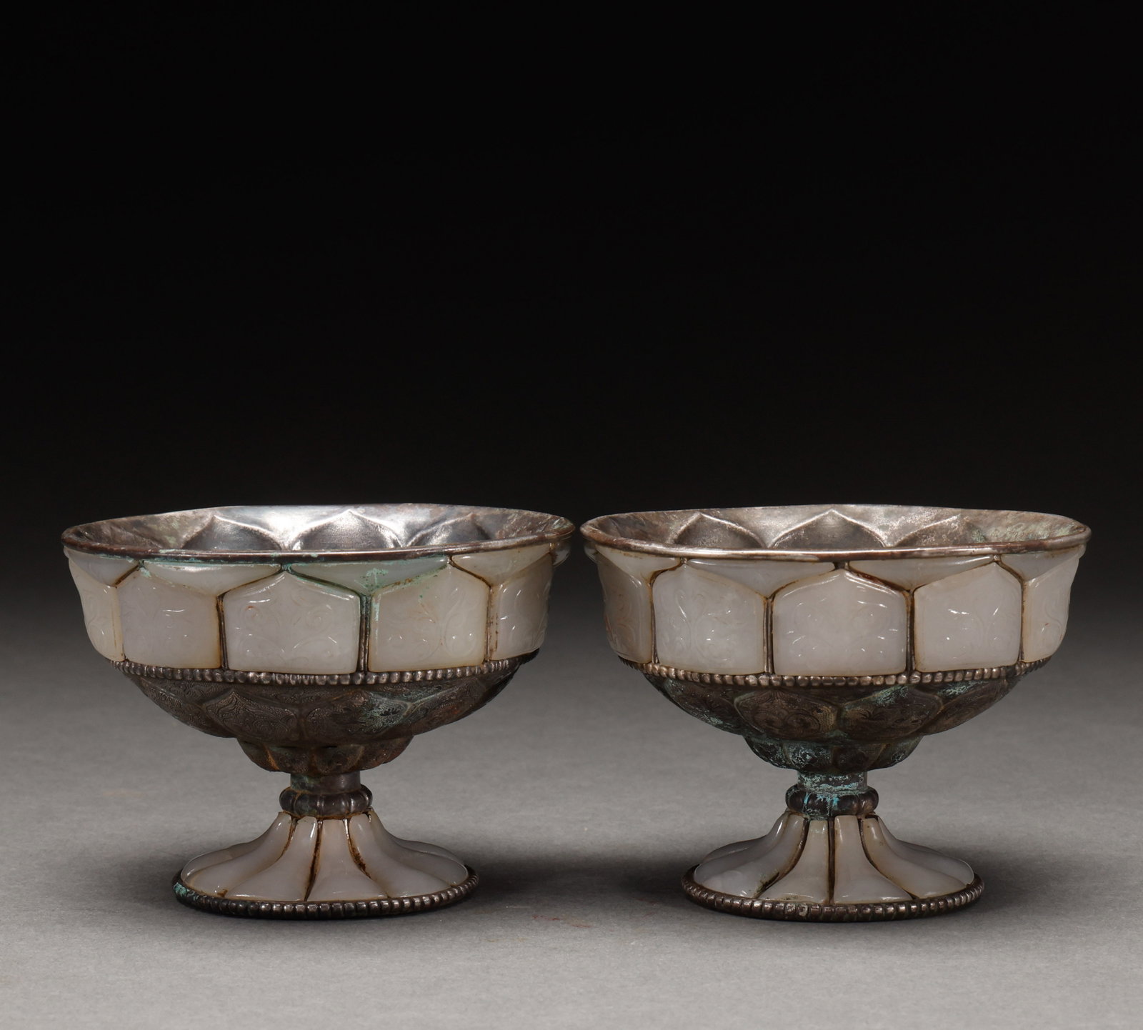 A pair of silver inlaid Hotan Jade cups before the Ming Dynasty: A pair of silver inlaid Hetian jade lotus petal goblets, 7.2 ?? 10cm in size and 444g in weight. The carved white jade lotus petal is spliced with carved silver body, which is a complete set of luxuri