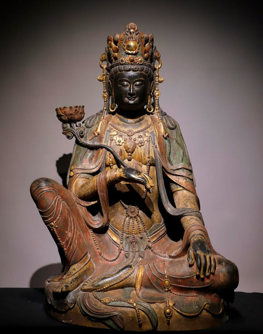 Before the Ming Dynasty, the blue stone painted statue of Guanyin holding a lotus was sitting: Pre-Ming Painted Bluestone Seated Guanyin Holding a Lotus. Well-proportioned in form and flowing in line, the piece stands 100 cm tall, is 66 cm wide, and is 53 cm thick. The features are reverent and