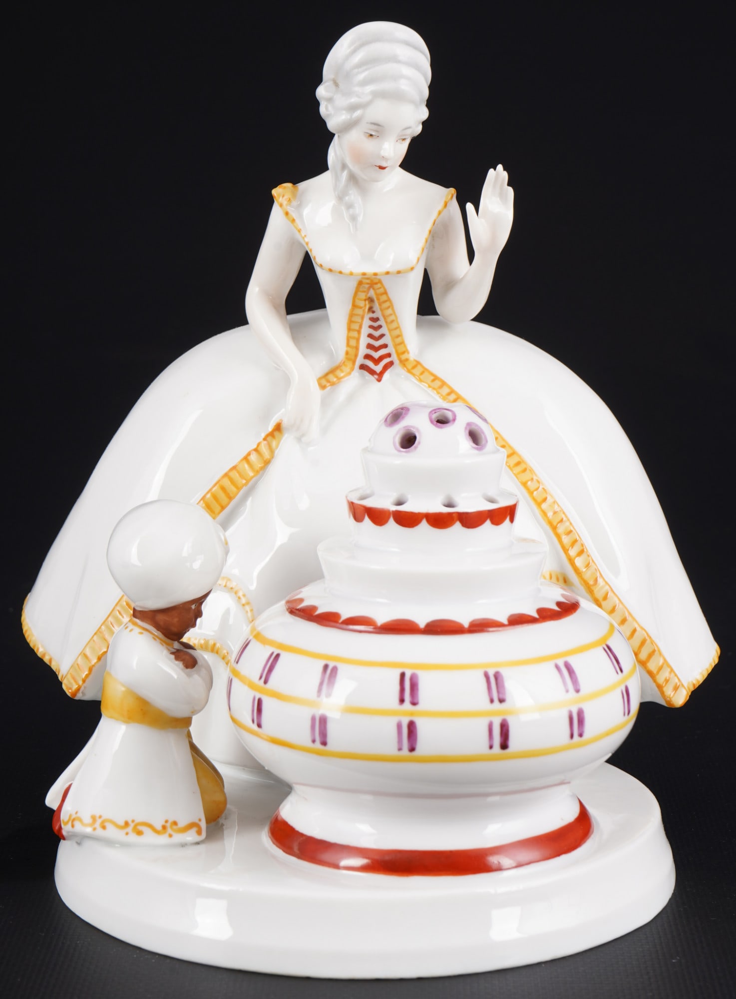 Heubach Aladin figural smoke eater,: porcelain, green company mark, standing lady in a crinoline skirt looking down at a vessel, next to her kneeling Moor, model no. 12723, H 19.5 cm x W 17.5 cm x D 17.5 cm