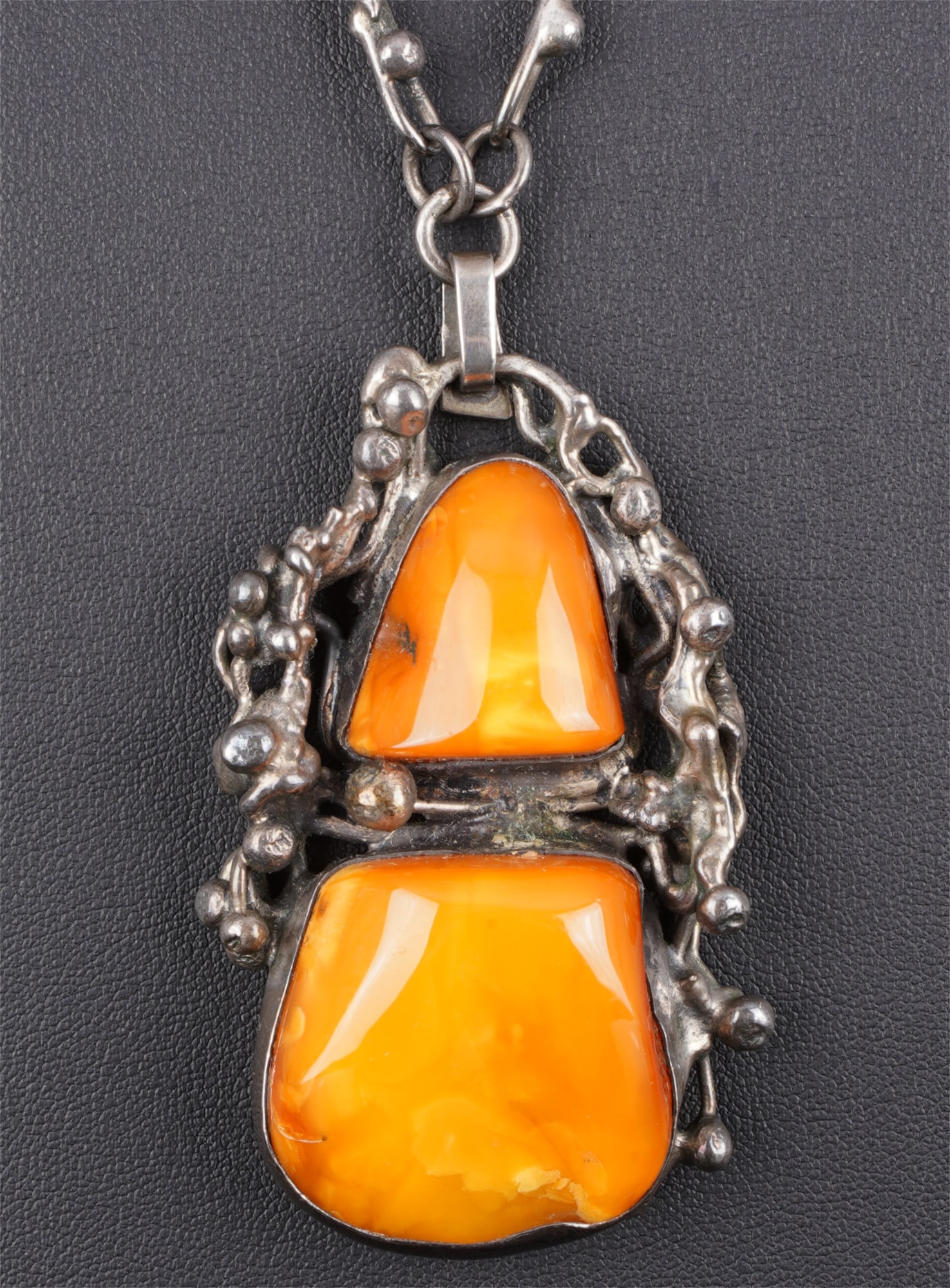 Large amber pendant with necklace: The pendant features two warm-toned amber stones, artistically mounted in what appears to be silver. The striking chain with its handcrafted links further emphasizes the piece's artistic character. Pe