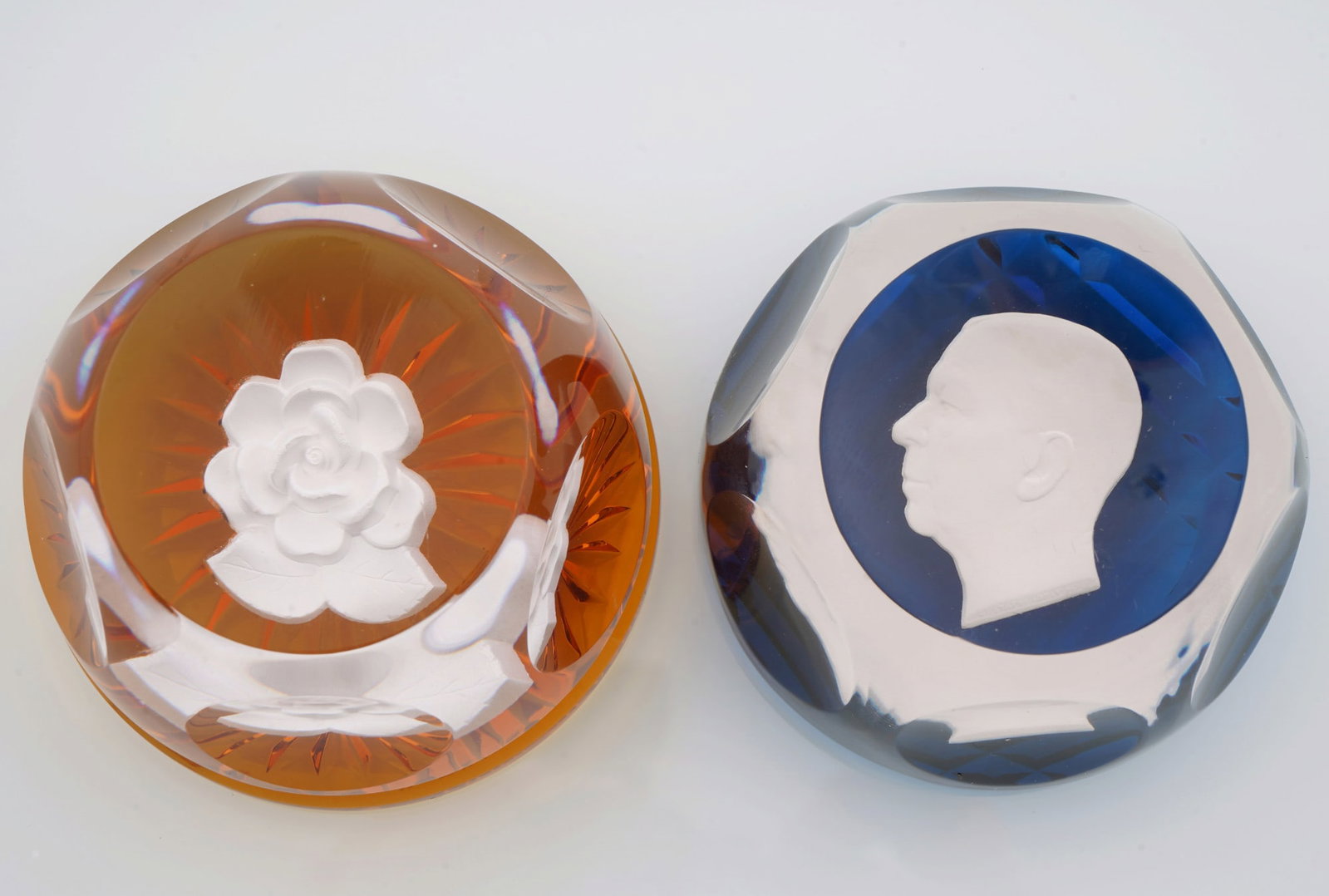 Bayel and D'Albert paperweights portrait and flower: Colorless crystal glass, two paperweights with orange and blue bases with white motifs, France D'Albert with portrait of Gustav VI H 5 cm x D 6.8 cm and France Bayel with flower H 5 cm x D 7.2 cm,