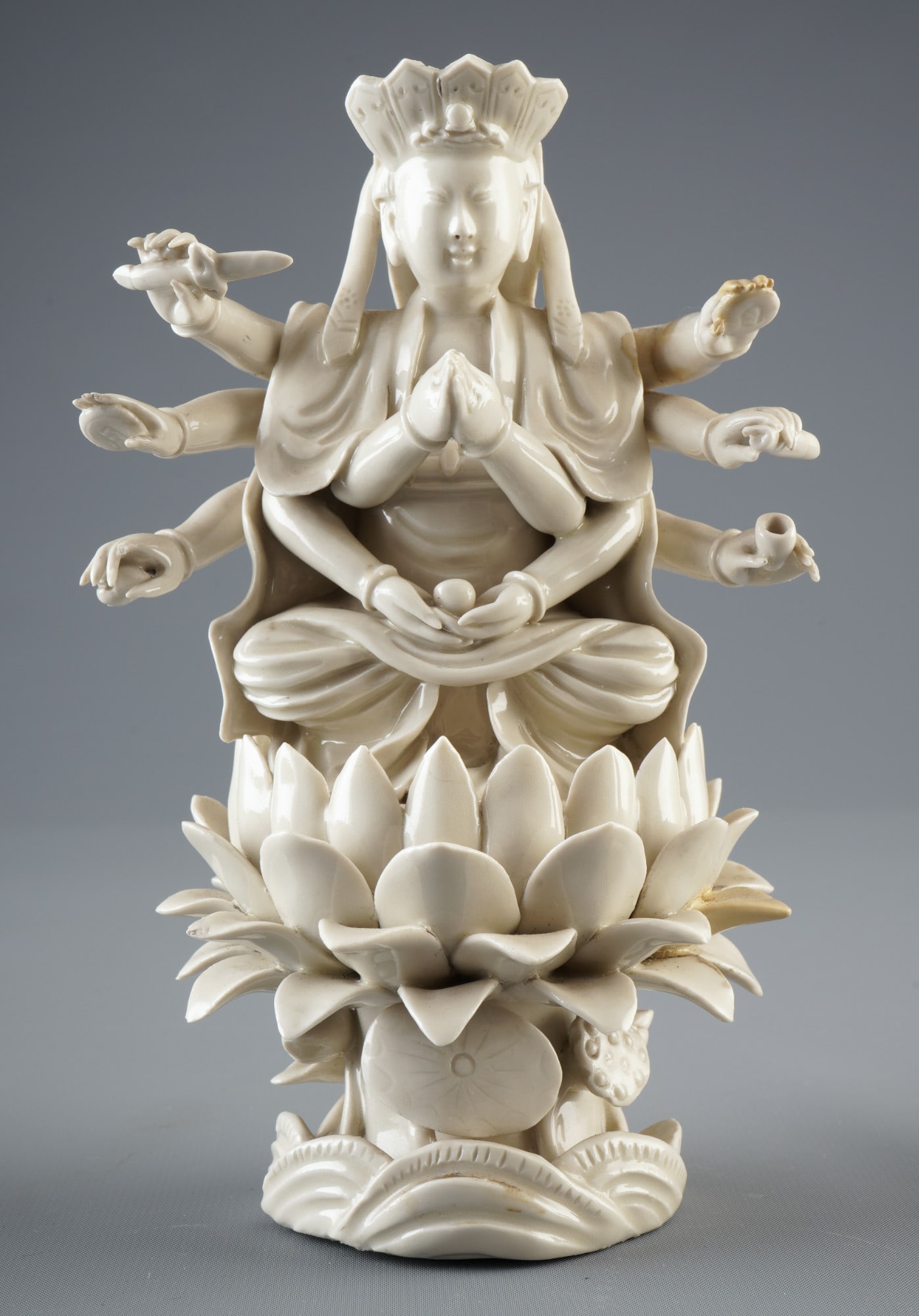 Dehua-Guanyin figure with ten arms, China, Qing Dynasty: Porcelain, China, Qing Dynasty (1644-1911), Dehua-Guanyin figure with ten arms, seated on a lotus base, holding various mudras or attributes, H 19.8 cm x W 12 cm x D 10 cm, minor damage and repairs to