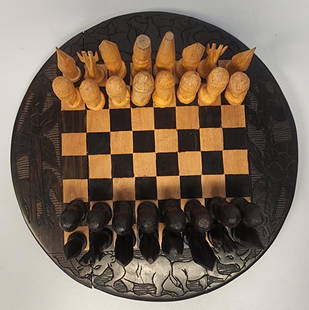 Wood Carved Chess Set: Artist Unknown Wood carved chess set with complete set of pieces Chess pieces are carved in African-style figures Board Dimensions: 10.5 H x 10.5 W x 1 D in All proceeds from our auctions support