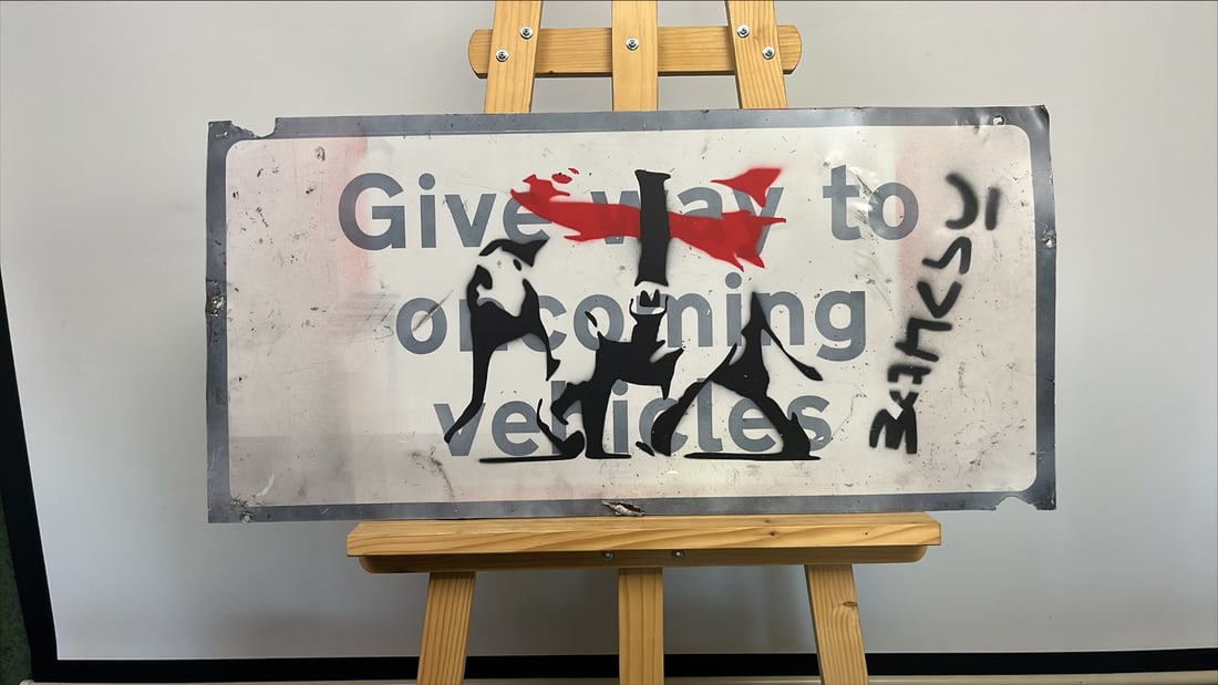 BANKSY - Stencil/Spray on Metal Old Traffic Direction Road Sign - Dismaland WSM: Title: Heavy Weaponery. Stencil/Paint/Spray. Graffiti Art/StreetArt. On British Traffic Direction Road Sign Vintage. This is being sold as attributed to Banksy as pest control will not issue COA's for