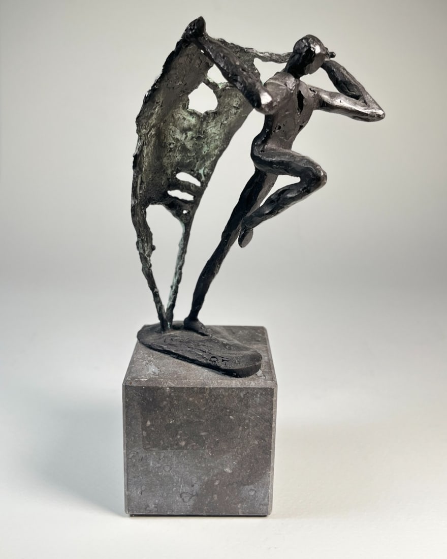 Klaas van Berg - Bronze Sculpture - Hand-signed: Against the Wind, Klaas van den Berg – A bronze sculpture measuring 27 × 12 × 12 cm, mounted on a stone base. The figure leans into a sweeping, sail-like form, its posture suggesting both struggle