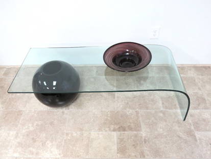 Style of Massimo Vignelli Waterfall Glass Coffee Table: A sculptural glass waterfall coffee table with spherical black glass ball support, small flake on underside of corner. Unmarked; 51" length, 20" width, 15" height.