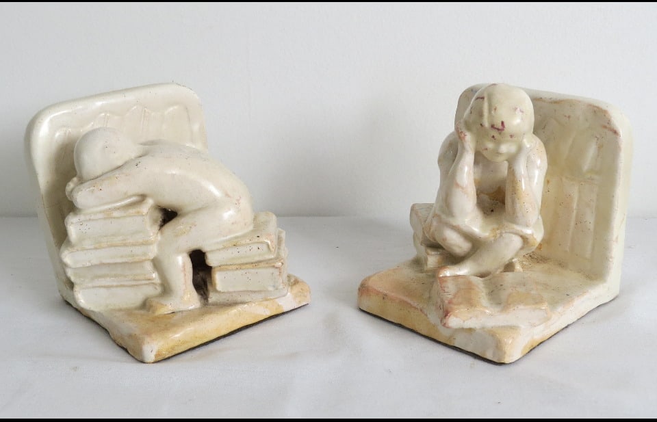 Art Deco Era Sculpted Pottery Bookends, Children Reading and Asleep: A pair of sculpted pottery Art Deco styled bookends featuring a young girl seated on a stack of books while reading one, while her male companion is sound asleep upon his own stack. Each 3.5" in heigh