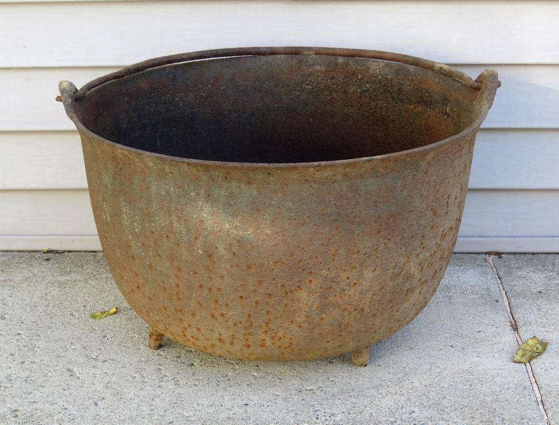 19th C. Cast Iron Tri-Footed Rendering Pot w/Gate Marks, Rattail Handle: A 19th C. cast iron tri-footed rendering pot or kettle with blacksmith forged swing handle featuring rattail ends. Pot is 20.5" diameter, and 13" in height to rim. Gate marks on bottom. Drilled at one