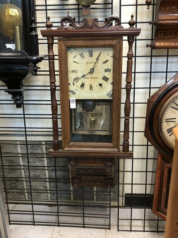 A SMITH JAMES BRIDGE EARLY WALL CLOCK, IN AS FOUND: A SMITH JAMES BRIDGE EARLY WALL CLOCK, IN AS FOUND CONDITION, HAS PENDULUM AND KEY, WHEN WOUND IT SOUNDS OFF, FACE HAS SOME WEAR, MEASURES 34" HIGH. LOOKS LIKE TOP OF TOP IS MISSING A PIECE. FROM SHOP