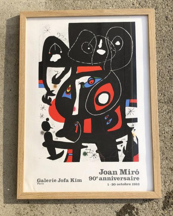 JOAN MIRO FRAMED 1983 GALLERY POSTER, LIGHT WATER STAIN: JOAN MIRO FRAMED 1983 GALLERY POSTER, LIGHT WATER STAIN BOTTOM LEFT CORNER. POSTER MEASURES 30" X 22", NICE BLONDE OAK FRAME.