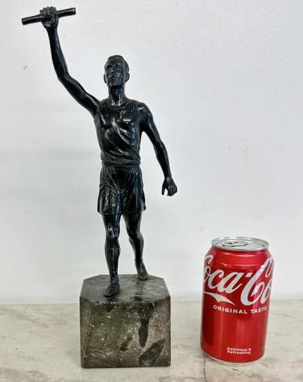 Circa 1910 white metal statue of male athlete holding baton, some of the black finish is worn in (1 of 3)