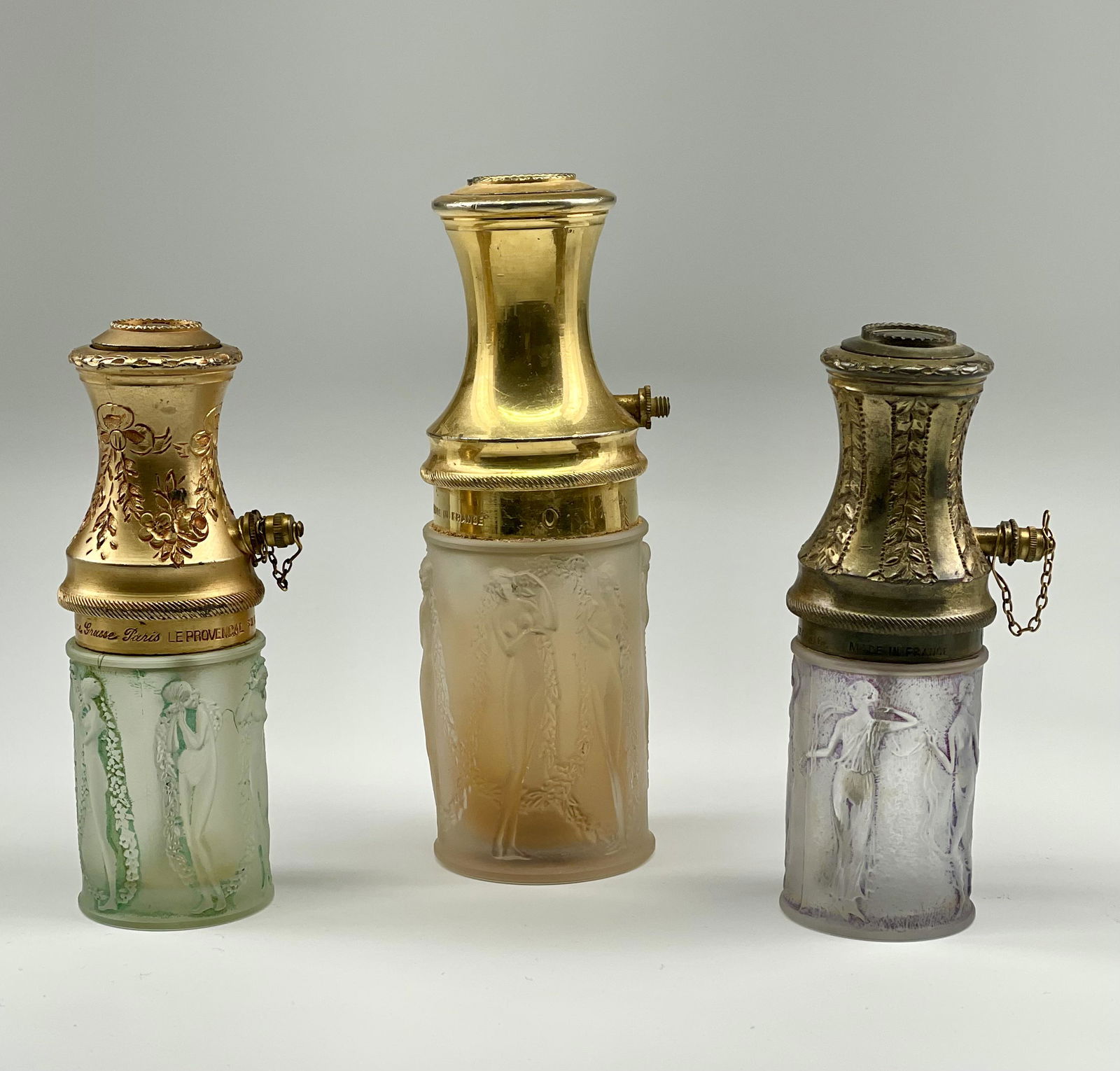 Three R. Lalique Atomizers Le Parisien Nude, Garland, Maidens: Lot of three. 1) Atomizer. â€œR. Lalique Made in France” embossed at base. Le Parisien. Gilt metal top. Frosted glass base with nudes and garland. Condition: Gilt finish crackling, chain mis