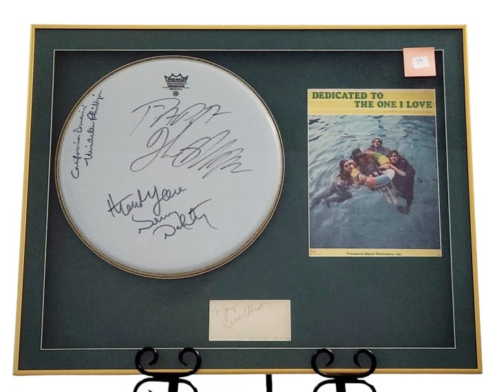 Cass Elliot Mamas & Papas Autographed Memorabilia: Framed collection of Mamas & Papas' memorabilia including a Remo snare head signed by members of the band, a Cass Elliot signature, and a song book for "Dedicated to the One I Love". Professionally mo