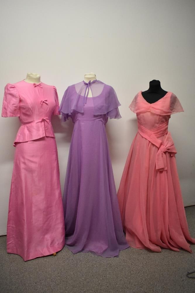 A 1950s pink evening gown with full skirt, a 1960s pink gown with bows to bodice and a 1970s John: A 1950s pink evening gown with full skirt, a 1960s pink gown with bows to bodice and a 1970s John Charles dress in mauve.