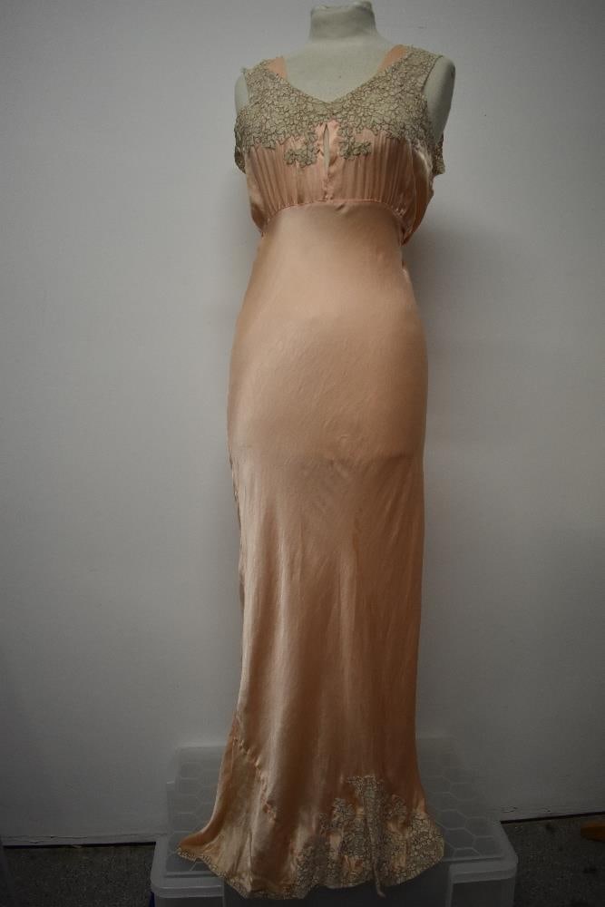 An Art Deco pale pink bias cut nightdress, having beautiful lace to bodice and hem, tie fastening to: An Art Deco pale pink bias cut nightdress, having beautiful lace to bodice and hem, tie fastening to waist, low cut back and peep hole to bodice medium to larger size.