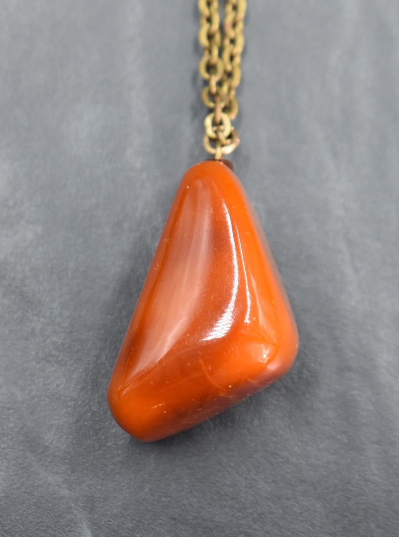A large amber style pendant of triangular form on a yellow metal chain, 30.7g: A large amber style pendant of triangular form on a yellow metal chain, 30.7g