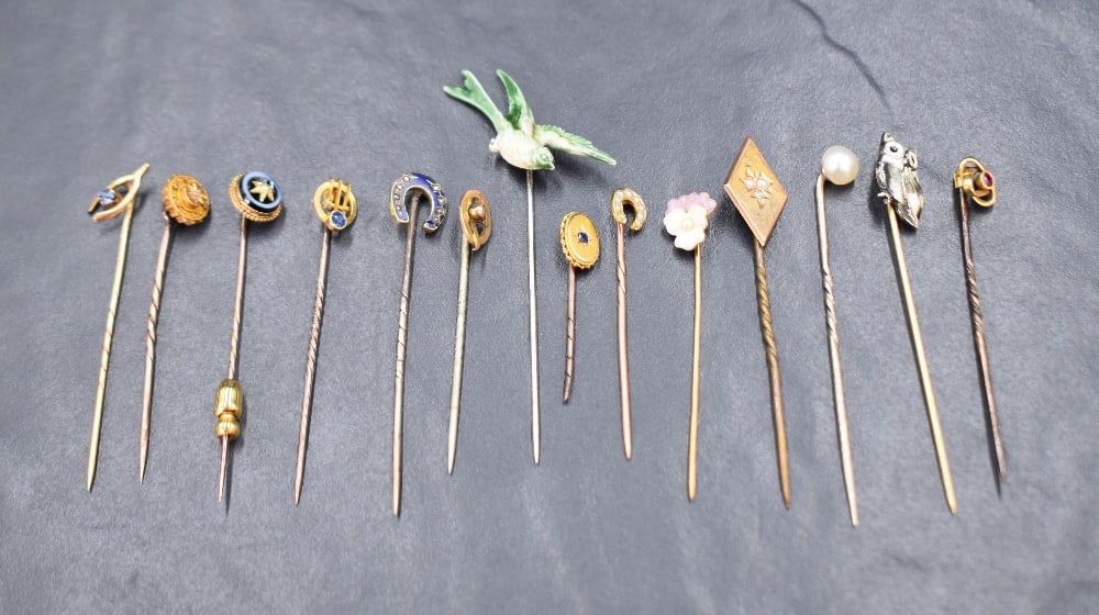 A collection of yellow metal stick pins including an enamel and diamond set horse shoe, a seed pearl (1 of 1)