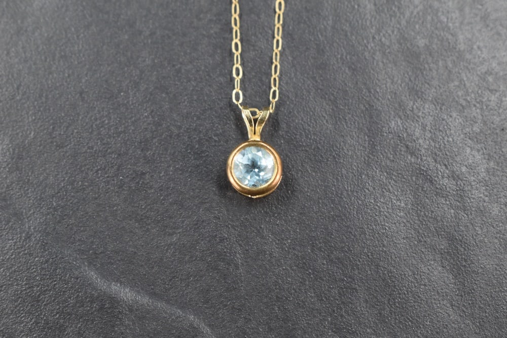 A small blue topaz pendant in a 9ct gold collared mount on a 9ct gold fine link chain, approx: A small blue topaz pendant in a 9ct gold collared mount on a 9ct gold fine link chain, approx 18' & 0.8g