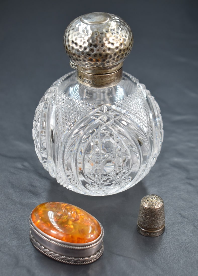 A 20th century silver mounted cut glass scent bottle, having rubbed marks for Chester, along with: A 20th century silver mounted cut glass scent bottle, having rubbed marks for Chester, along with a silver amber set pill box marked 925 and a thimble